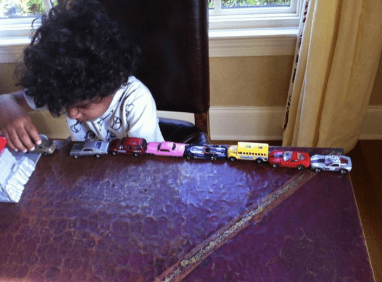 Hudson as a young child, lining up toy cars on a table